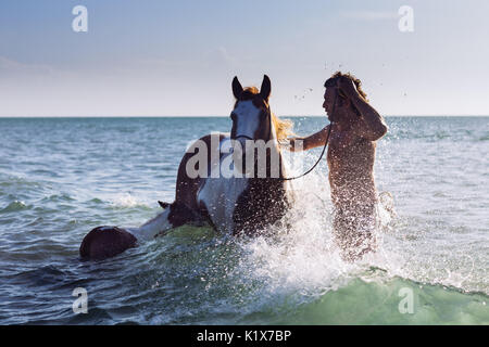 Un uomo di lavaggio di un cavallo e la sua lettiera in mare di Jericoacoara, Ceará, Brasil Foto Stock