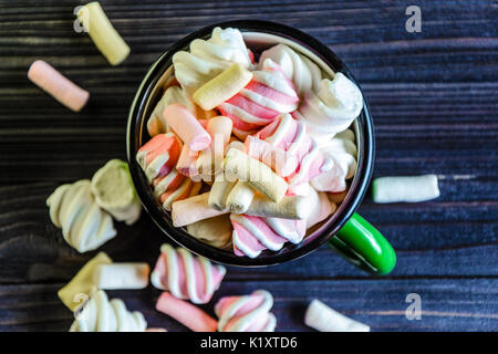 Il verde smaltato tazza è riempita con un multicolore marshmallow su tavoli in legno nero vista superiore Foto Stock