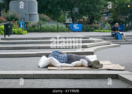 Un uomo non identificato, presumibilmente senzatetto, dormire durante la tarda mattinata in Union Square Park a Manhattan, New York City Foto Stock