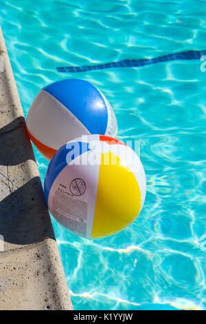 Palline da spiaggia colorate galleggiano in una bella piscina blu cristallo chiaro in una calda giornata estiva Foto Stock