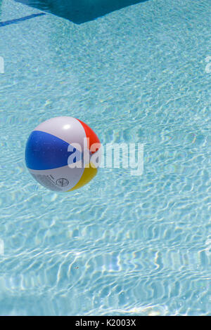 Beachball colorato che galleggia in una bella piscina blu cristallo chiaro in una calda giornata estiva Foto Stock