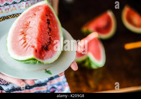 Anguria sfondo. Ragazza in un colorato estate shirt tenendo una piastra con una grande fetta di cocomero contro uno sfondo di una tabella sfocate con sl Foto Stock