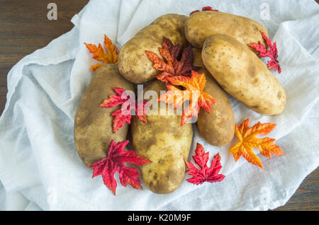 Still Life 6 patate coperto con foglie di autunno e impilati su un panno bianco visto dal di sopra Foto Stock