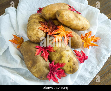 Still Life 6 patate coperto con foglie di autunno e impilati su un panno bianco visto dal di sopra Foto Stock