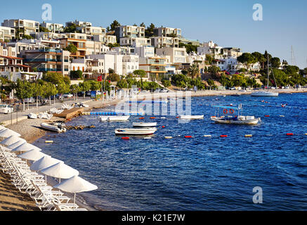 Alberghi e bianchi ombrelloni vicino a laguna con barche sulla spiaggia di bodrum, Turchia Foto Stock