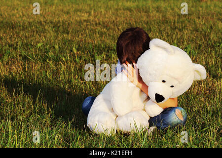 Triste Bambino seduti all'aperto e abbracciando Teddy bear Foto Stock