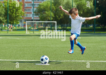 Ragazzo giocatore di calcio con un salto prima di un calcio sulla sfera Foto Stock