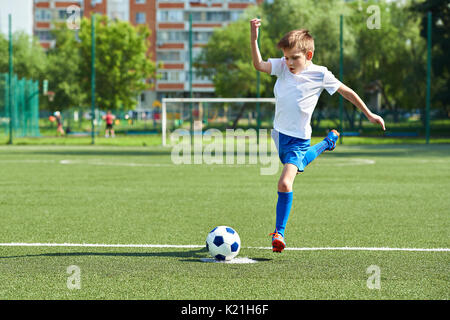 Ragazzo giocatore di calcio con un salto prima di un calcio sulla sfera Foto Stock
