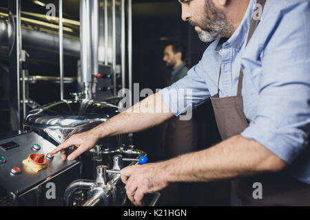 Vista ravvicinata di birraio maschio lavora con attrezzature industriali presso la birreria Foto Stock