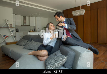 Coppia di mezza età in formalware nel loro appartamento di città con un uomo che serve caffè per una donna Foto Stock