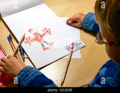 Ragazzo con gli occhiali al banco ammirando la sua immagine di spiderman disegnato con matite colorate su conferenza nota di rottami di carta Foto Stock