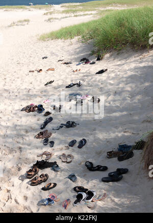 Sandali, infradito & scarpe a sinistra nella sabbia dai piedi nudi beachgoers. Foto Stock