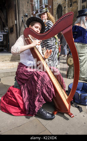 Giovane donna suonare l'arpa in Lincoln, durante il 2017 Steampunk Festival di asilo, città di Lincoln, Lincolnshire, Regno Unito Foto Stock
