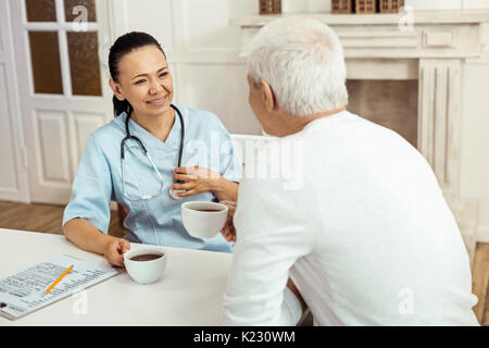 Gioioso caregiver positiva avente il tè con la sua paziente Foto Stock