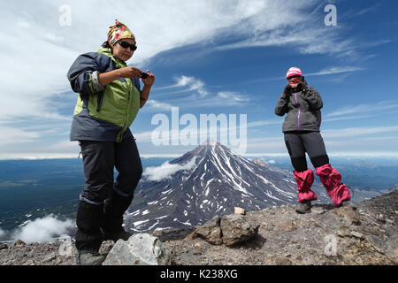 Escursioni in montagna - due donne giovani turisti stand della cima del cratere sommitale del attivo vulcano Avachinsky sullo sfondo del cono del vulcano popolare Koryak Foto Stock