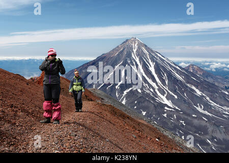 Due giovani donne i turisti sono a piedi lungo un percorso escursionistico di montagna sul bordo del cratere del vulcano attivo, fotografando paesaggio vulcanico su Kamchatka. Foto Stock