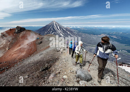 Gruppo di escursionisti che sale lungo il bordo del cratere sommitale del attivo vulcano Avachinsky sullo sfondo del cono del vulcano popolare Koryak sulla penisola di Kamchatka. Foto Stock