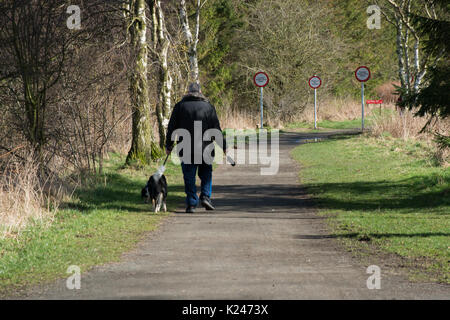 Un solo escursionista che trasporta il sacchetto di escrementi al contenitore fornito e con avvisi di sicurezza dell'autorità locale sul percorso laterale del paese Foto Stock