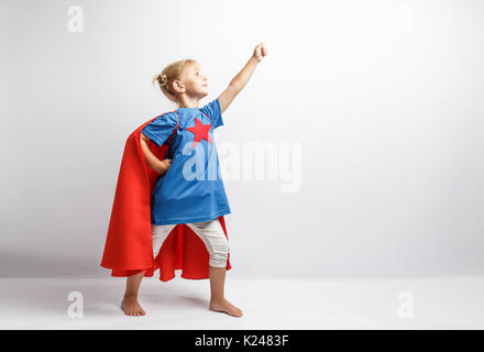 Bambina vestito come supereroe in piedi accanto al muro bianco Foto Stock