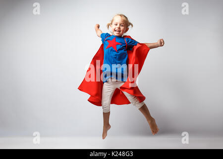 Sono molto eccitato bambina vestito come supereroe saltando a fianco del muro bianco Foto Stock