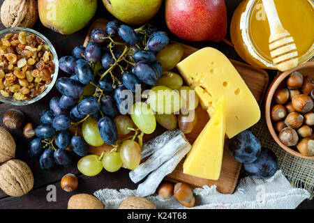 Autunno insieme di prodotti: l'uva, le noci, le nocciole, le prugne, miele, formaggio, uvetta, pere, mirtilli rossi secchi su uno sfondo di legno. Vista dall'alto. Foto Stock