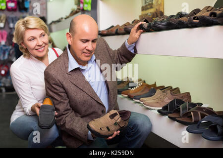 Donna matura aiutando il marito scegliere comode scarpe mans nel negozio di moda Foto Stock