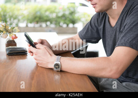 Giovane uomo caucasico controllo social news update e messaggio sul telefono intelligente al cafe. avviare piccoli imprenditori lavora con telefono mobile a Foto Stock