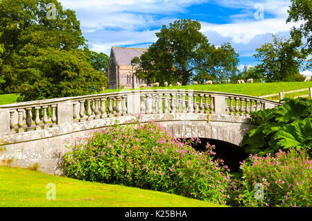 Una scena pastorale nella motivazione di Brough Hall, North Yorkshire, con pecore al pascolo, una deliziosa vecchia chiesa e un diciottesimo secolo bugnato in pietra arenaria bridge. Foto Stock