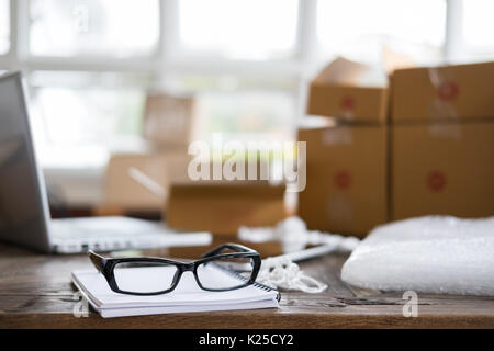 Notebook, occhiali al lavoro di start up, titolare di una piccola azienda, freelance, imprenditore, SME venditore. cartone scatola di pacchi di prodotti da consegnare Foto Stock