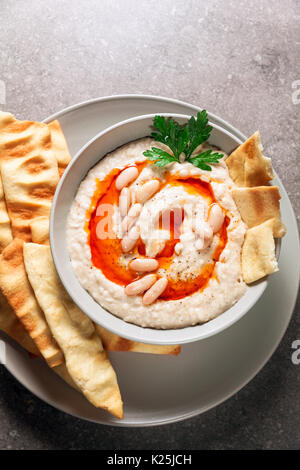 Hummus di fagioli bianchi con olio piccante del peperoncino e fatti in casa pani croccanti su una pietra grigia tabella Foto Stock