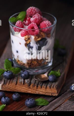 Vetro con frutta fresca e bacche surgelate e yogurt con foglie di menta Foto Stock