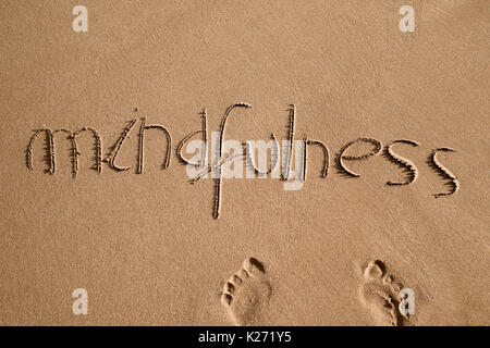 Alta angolazione della parola mindfulness scritto nella sabbia di una spiaggia e una coppia di impronte umane Foto Stock