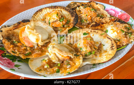 Closeup deliziosa le capesante alla griglia con burro e salsa piccante sul guscio sulla tavola di legno sfondo, Asian Thai Seafood. Foto Stock