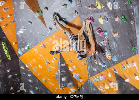 Giovane maschio rocciatore sul percorso impegnativo in piscina palestra di arrampicata Foto Stock