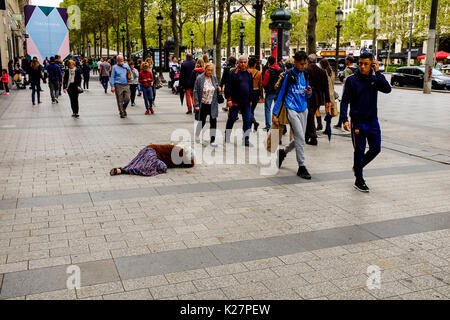 Una donna si trova sulla strada per l'accattonaggio denaro di fronte a persone e macchine ATM sugli Champs Elysees, Paris, Francia il 15 settembre 2016. Foto Stock