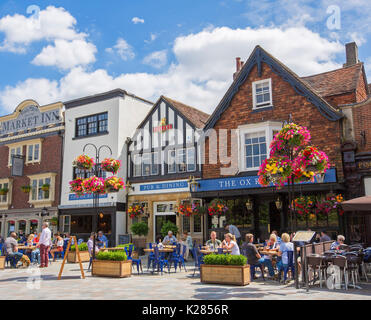 Diners a tavoli all aperto accanto a Ox Row Inn nella storica piazza del mercato adornata con cestelli appesi dei fiori sotto il cielo blu a Salisbury, Inghilterra Foto Stock