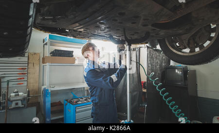 Lavoratore svitamento meccanico di parti di automobile di fondo sotto la macchina sollevata Foto Stock