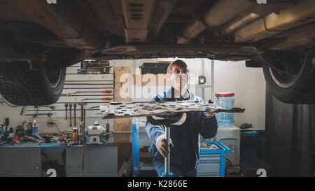 Maschio lavoratore caucasica - meccanico nel garage di automobili riparazione workshop - in auto sollevato Foto Stock