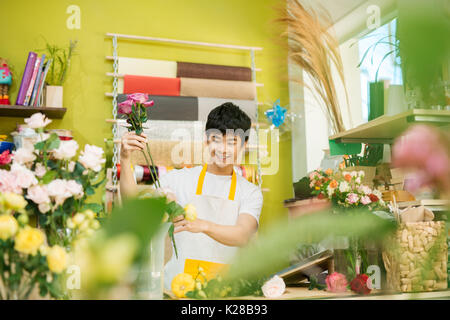 Sorridente giovani asiatici fioraio uomo rendendo bunch al negozio di fiori Foto Stock