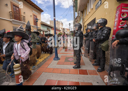 Giugno 25, 2017 Cotacachi, Ecuador: Riot Police in piedi da come il maschio di danze eseguite in giù lungo la strada verso la piazza principale Foto Stock