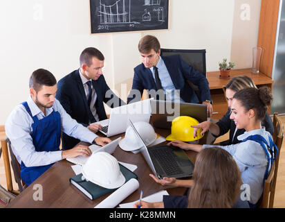 I giovani professionisti con i caschi e laptop avente riuniti in ambienti interni Foto Stock