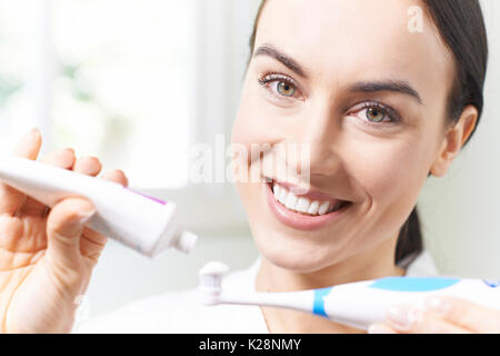 La donna la spremitura di dentifricio sullo spazzolino da denti elettrico nella stanza da bagno Foto Stock