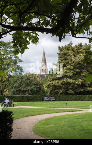 Un giovane e giovane uomo seduto rilassante nei giardini arboreto Nottingham, con la Chiesa di tutti i santi la guglia in background. Foto Stock