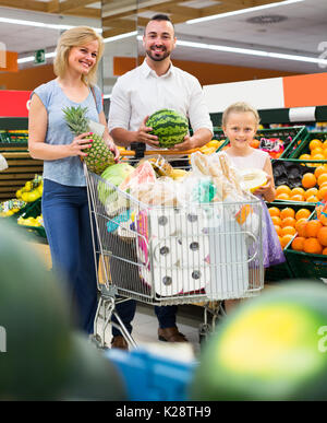 Giovani genitori sorridenti con piccola figlia nella sezione di frutta in ipermercati Foto Stock