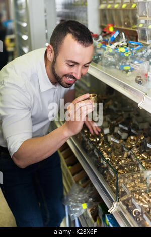 Uomo sorridente selezionando rubinetto metallico nel dipartimento di uso domestico Foto Stock