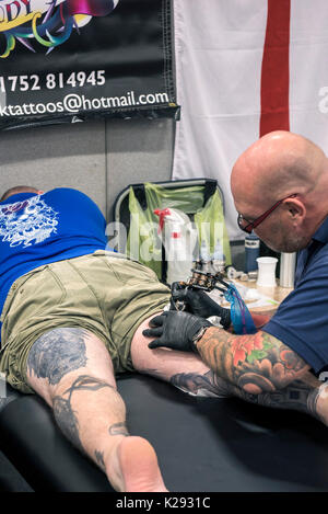 Tattoo - un uomo avente la sua coscia tatuati in Cornovaglia Tattoo Convention. Foto Stock