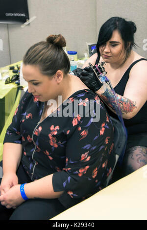 Cornovaglia Tattoo Convention - la femmina tattooist Laura G applicando un tatuaggio al retro di una femmina di cliente al Cornwall Tattoo Convention. Foto Stock