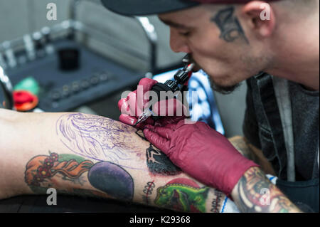 Tatuaggio. Un primo piano di tattooist Josh Docksey tatuaggio la gamba di un cliente al Cornwall Tattoo Convention. Foto Stock