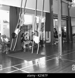 Anni sessanta, storico, immagine mostra due School girl ginnasti in tradittional kit PE eseguire una routine di artistico sul arrampicarsi sulle funi infront dei genitori, Inghilterra, Regno Unito. Foto Stock