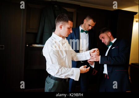 Groomsmen aiutare lo sposo a vestire e preparatevi per la sua cerimonia nuziale. Foto Stock